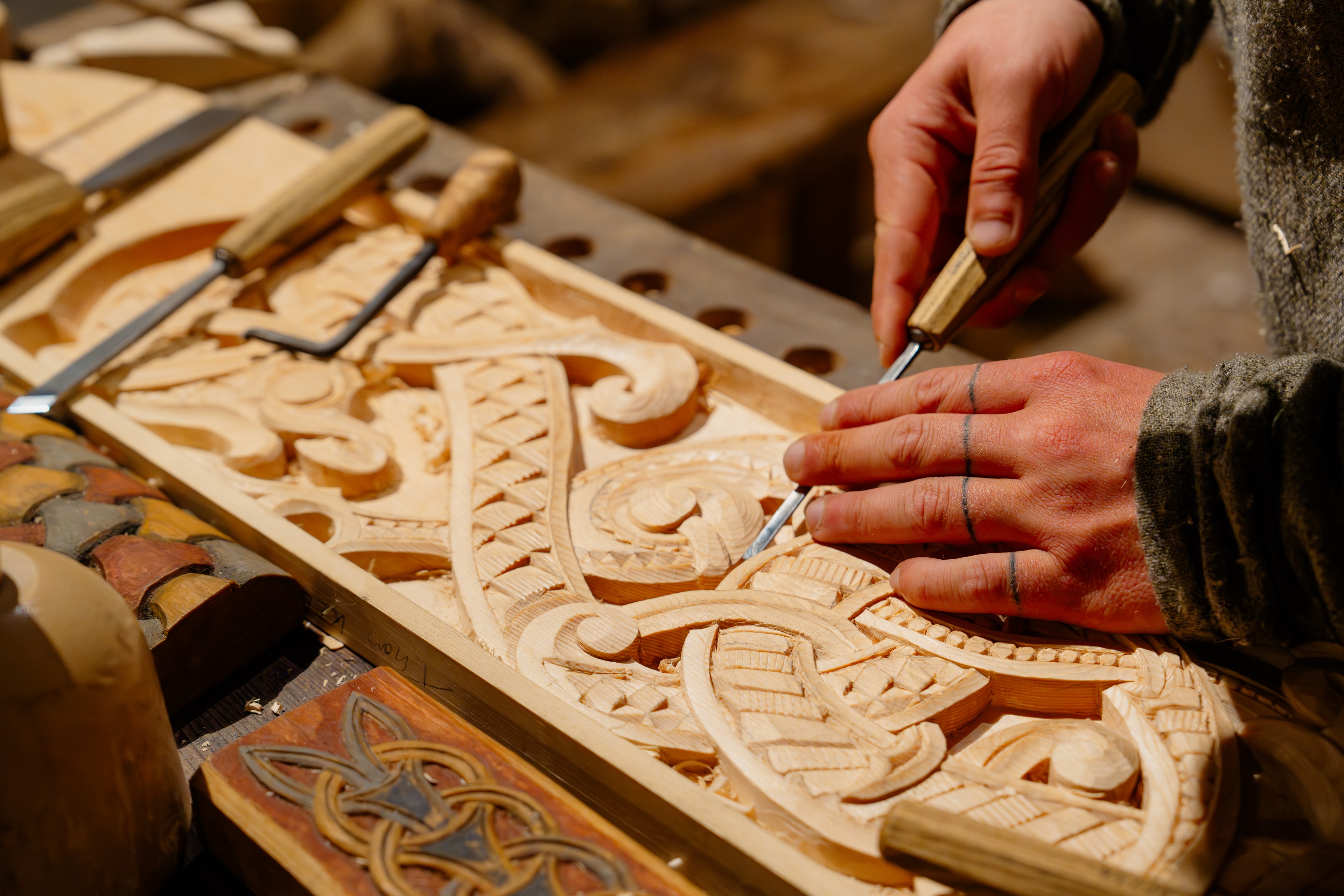 Hands carving intricate ornamental patterns into wood