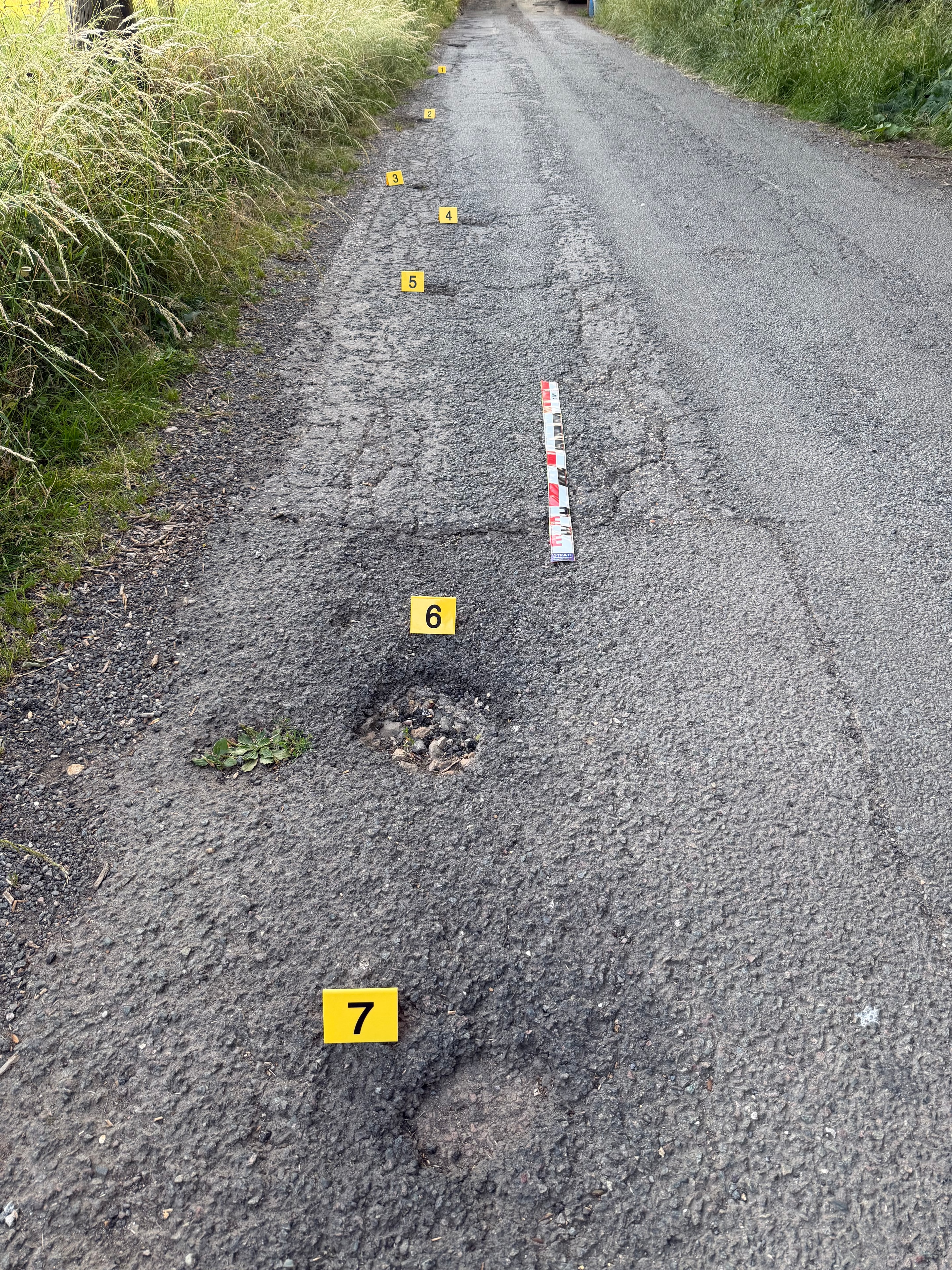 Numbered evidence markers documenting multiple potholes and surface defects on a local road during a volunteer survey